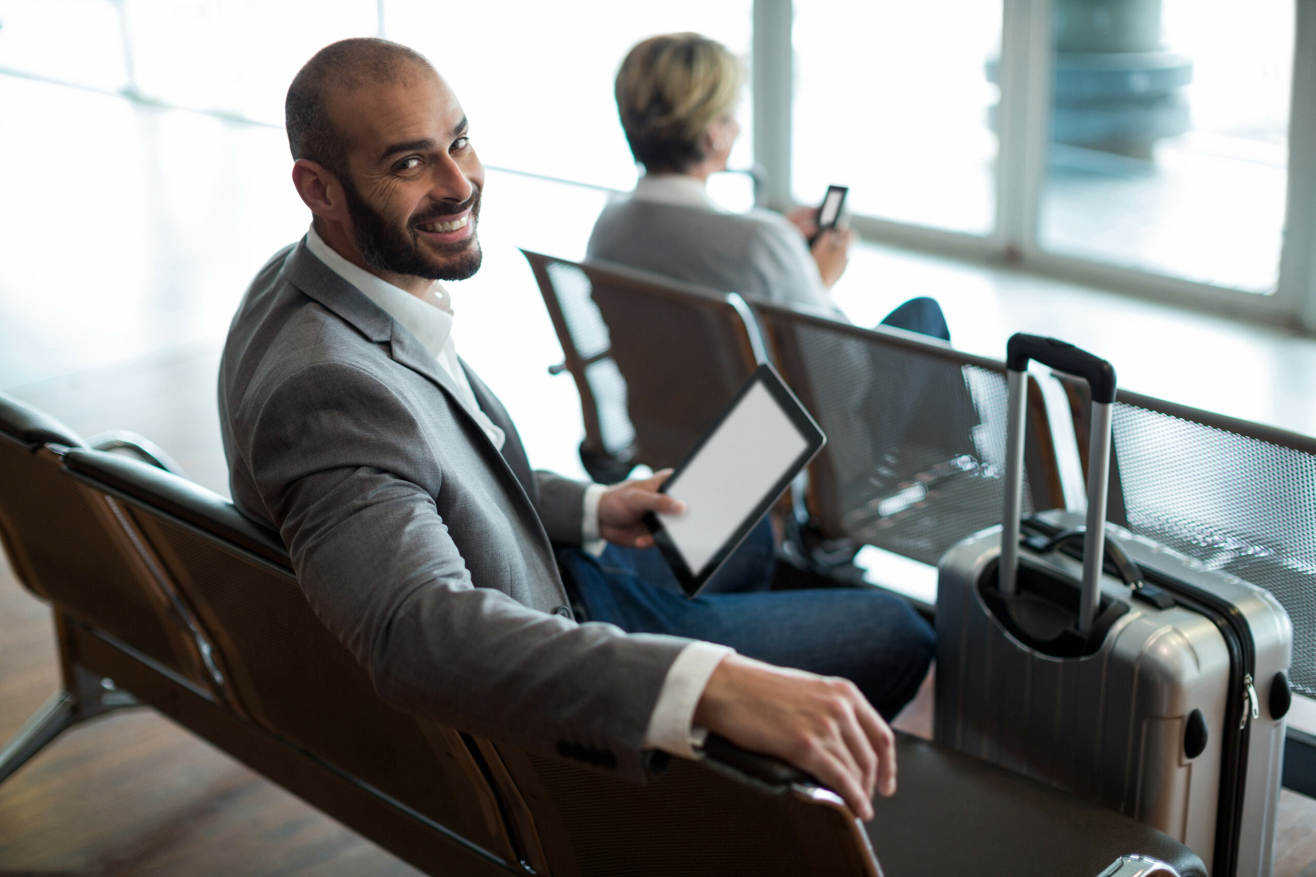 Hombre con una maleta y su smartphone en un aeropuerto ejemplificando Qué tan antes reservar un hotel para obtener el mejor precio