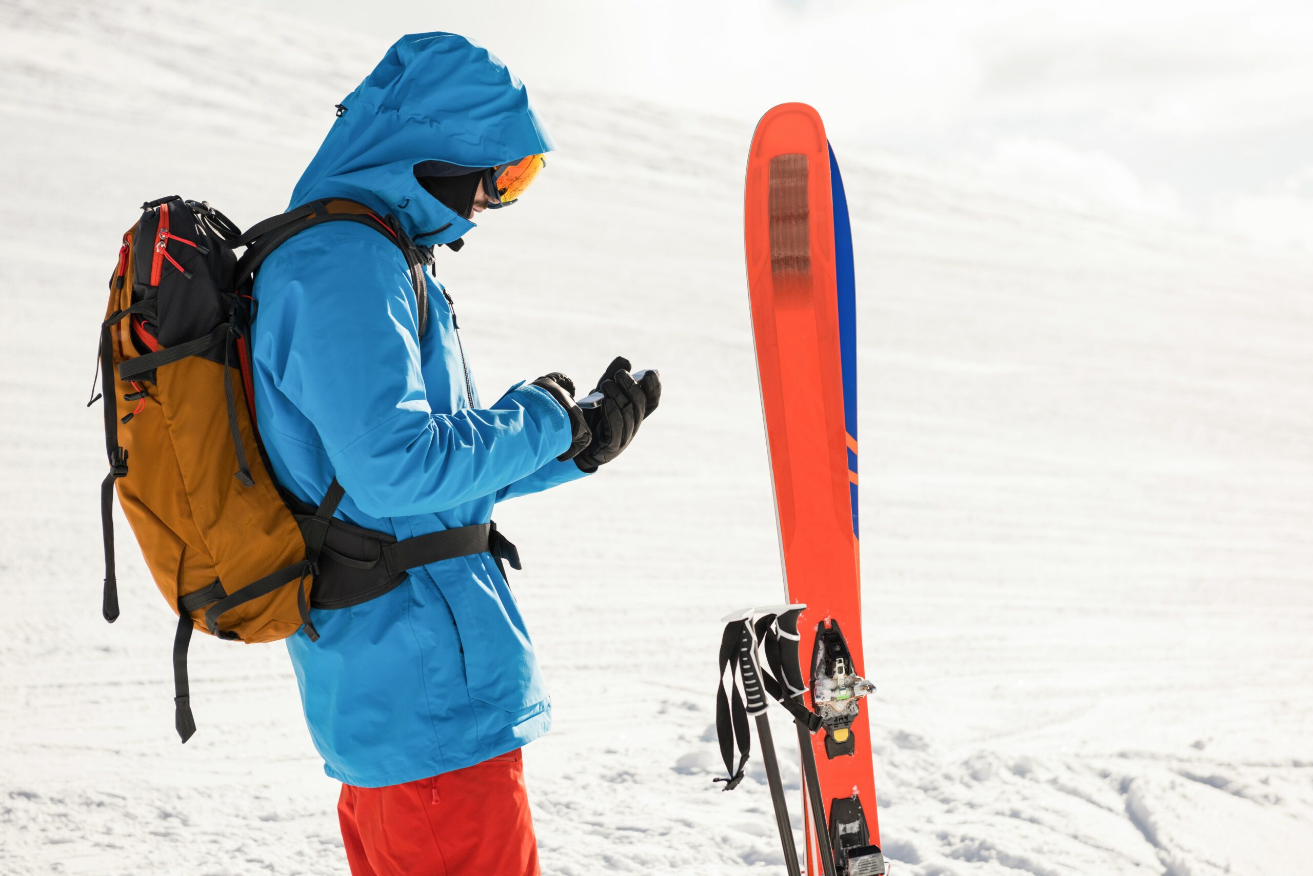 Hombre con equipo de esquí revisando en su celular la mejor aplicación para planificar un viaje